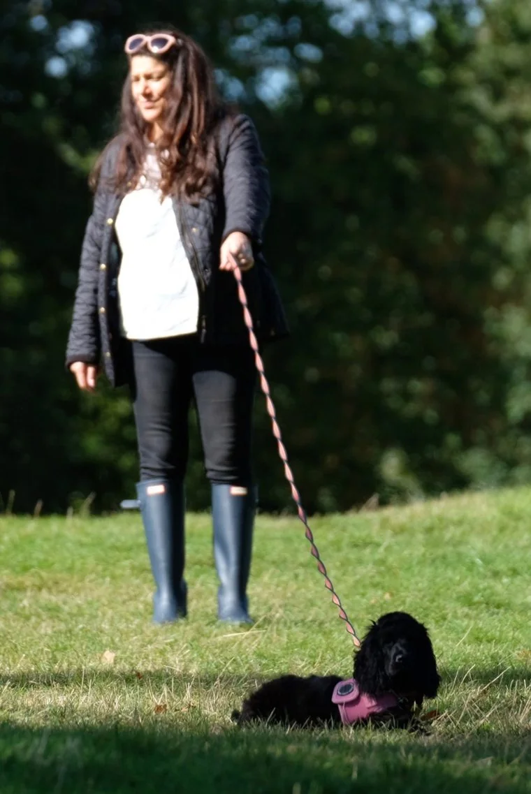 Claire in the park with a small black cocker spaniel on a lead, looking down at the dog